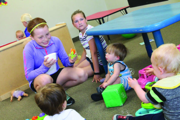 Girl in purple shirt making bubbles for three toddlers