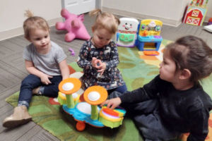 Mitchell group of three toddler girls playing with a colorful music instrument with toys in the background